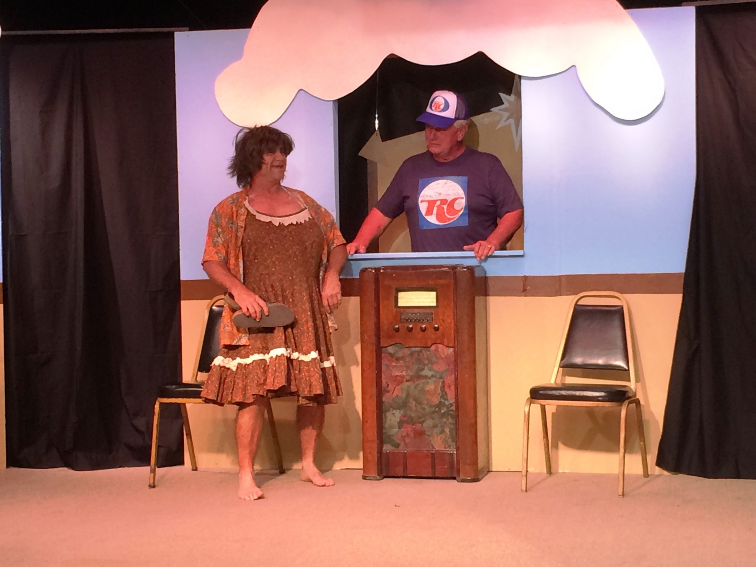 A male aA female actor wearing a dress speaks with a male actor wearing a t-shirt and hat and standing behind a counter